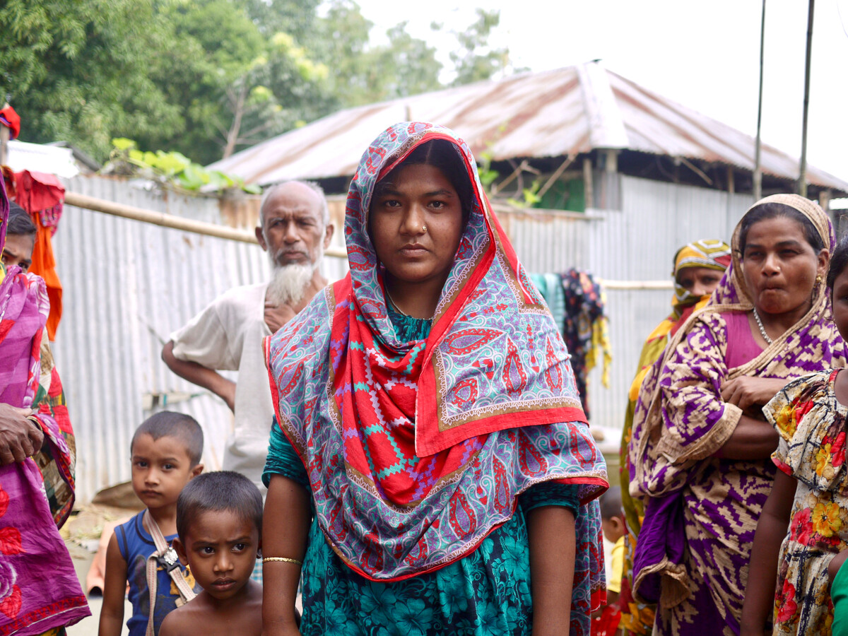 Eine Frau, umringt von anderen Frauen und Kindern, in farbenfroher Kleidung. Bild zeigt die Bewohner eines Dorfes in Bangladesch im Jahr 2017 nach einer Überschwemmung