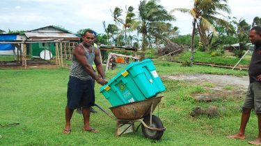 Übernimm ein Ehrenamt bei ShelterBox. Ein Mann transportiert eine ShelterBox in einer Schubkarre