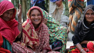 Frauen in Bangladesch sitzen zusammen und lachen während eines Evaluationsgesprächs mit einem ShelterBox Team.