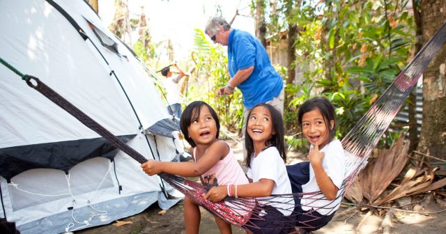 Drei Mädchen sitzen in einer Hängematte vor ihrem neuen ShelterBox Zelt