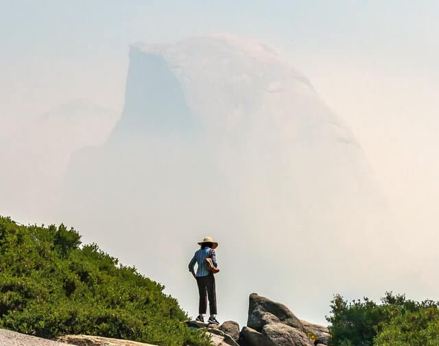 Frau steht im Rauch vor dem Half Dome im Yosemite Nationalpark