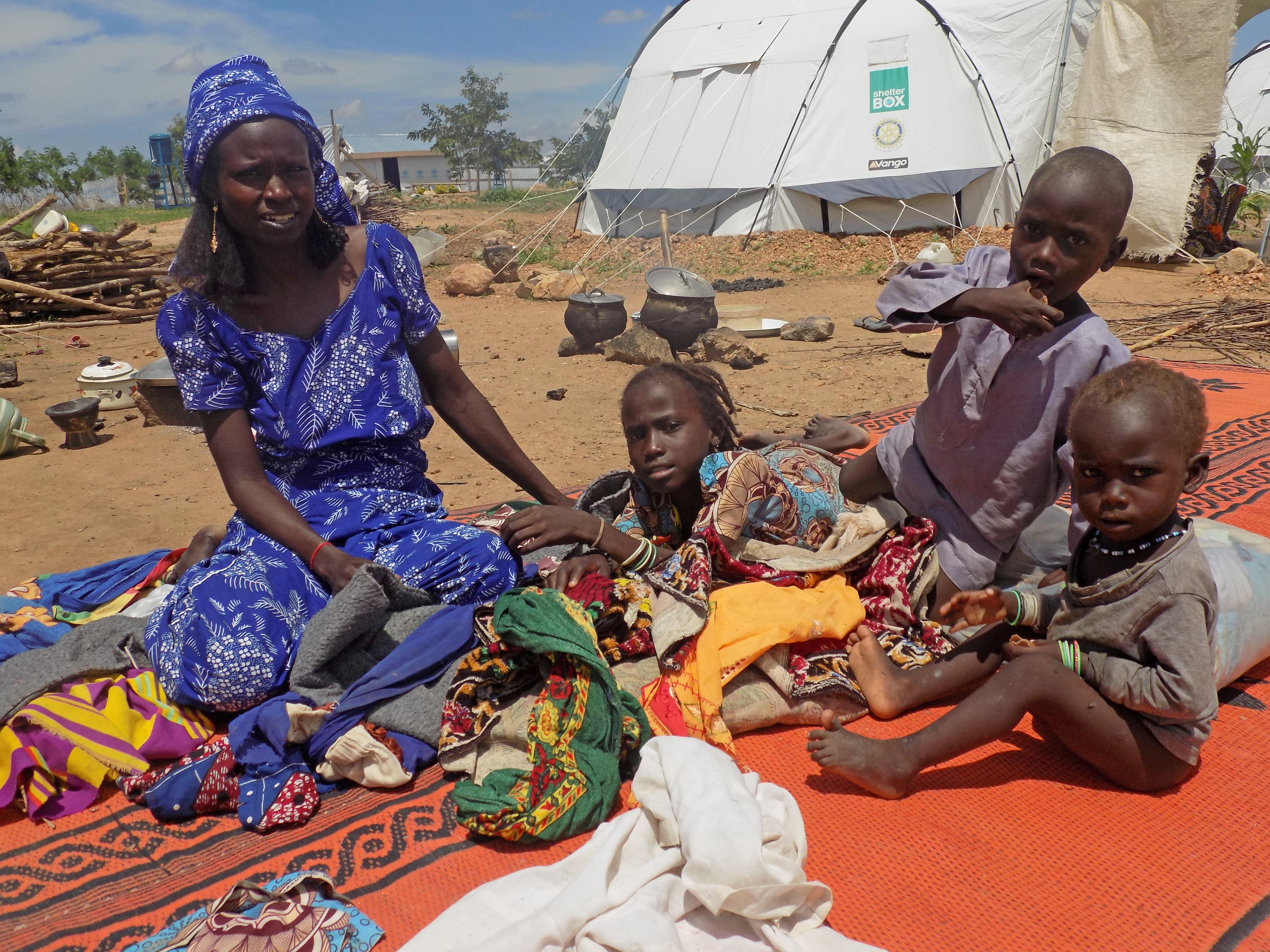 ShelterBox in Kamerun: Frau mit drei Kindern sitzen im Freien auf einer Decke.