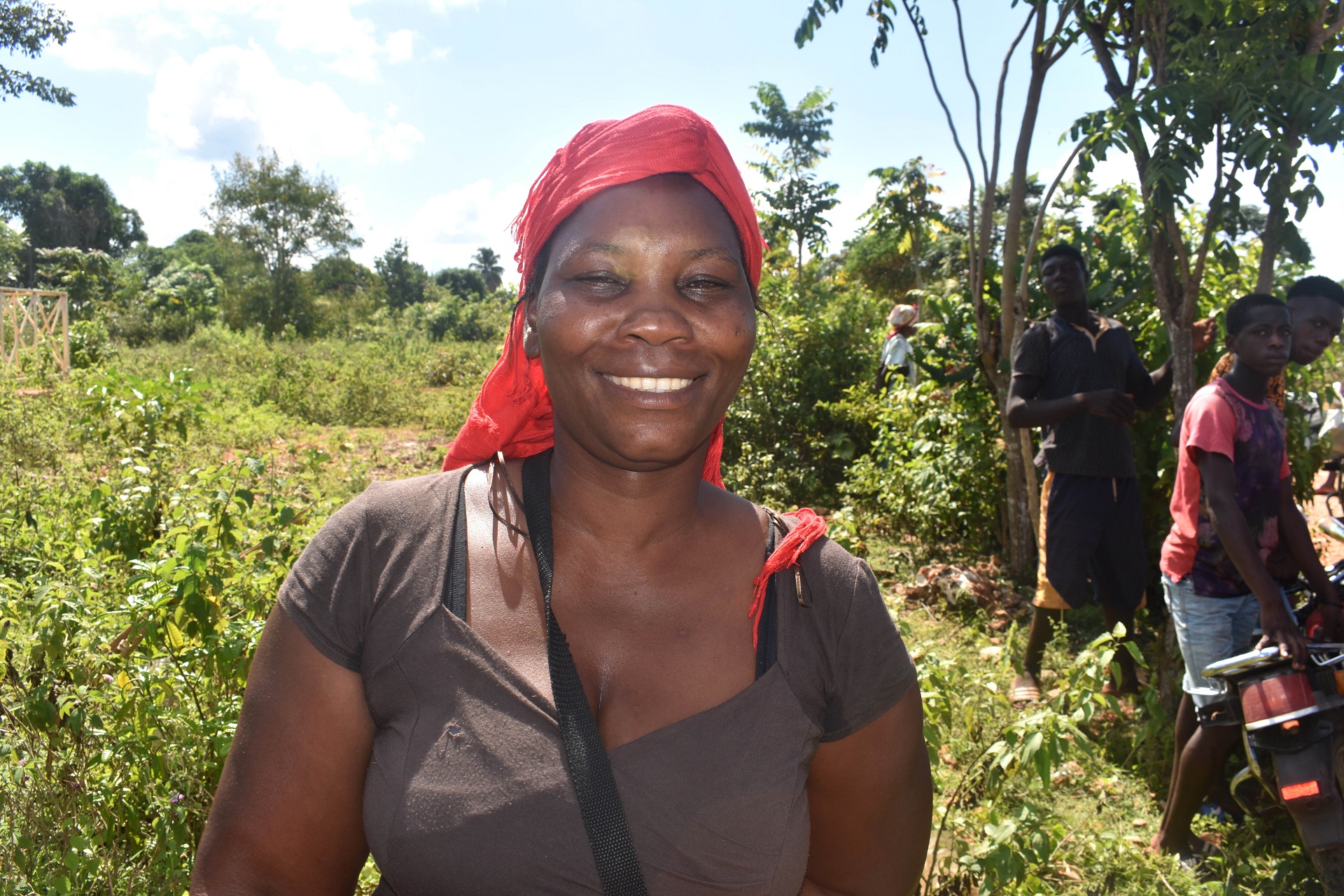 Nach dem Erbeben auf Haiti steht eine Frau mit einem roten Kopftuch lächelnd vor Palmen und Büschen.